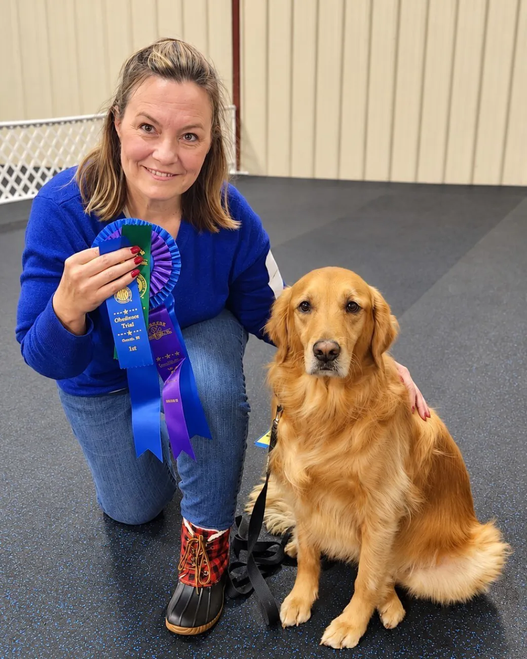 Hope, a golden retriever, sitting beside her handler Helen, who holds obedience ribbons